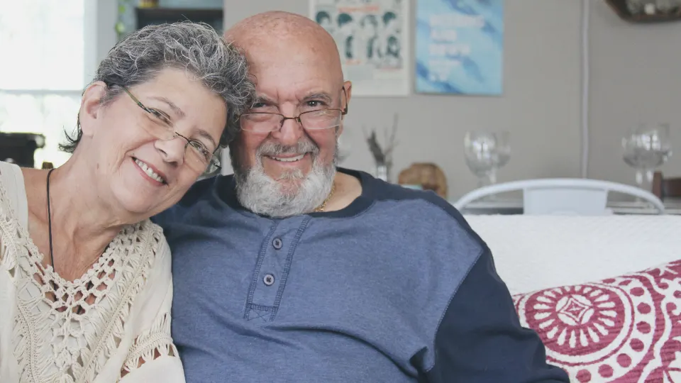 Casal de idosos sorrindo, abraçados em casa