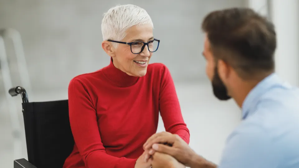 Senhora em cadeira de rodas conversando de mãos dadas com um rapaz