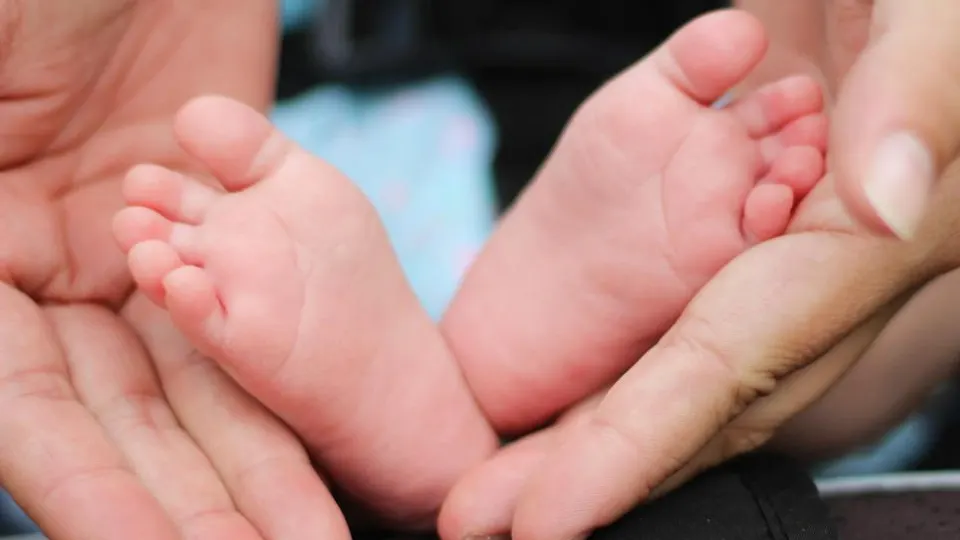 Pezinhos de um bebê apoiados nas mãos da mãe